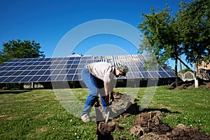 Man digging the ground with a showel in front of solar pannels.