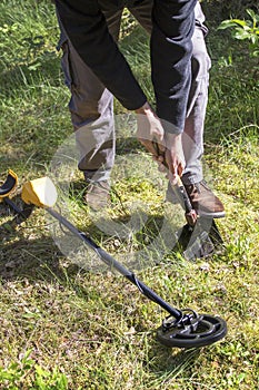 Man digs a hole in the ground using a shovel. Searching for militaries. The metal detector lies on the grass next to it.