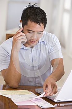 Man in dining room on cellular phone using laptop