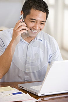 Man in dining room on cellular phone using laptop