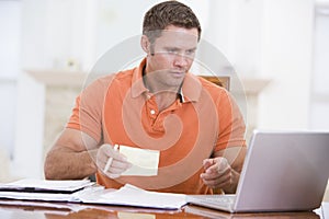 Man in dining room with laptop holding paperwork