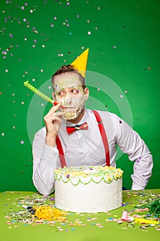 Man with dirty face from cake blowing party horn in studio