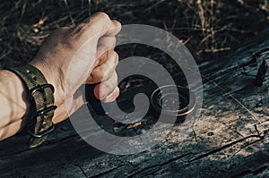 Man dirty hand holds a knife, a compass on an old log in forest.Survival