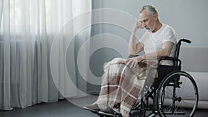 Man with disabilities sitting in wheelchair and thinking about illness, disease