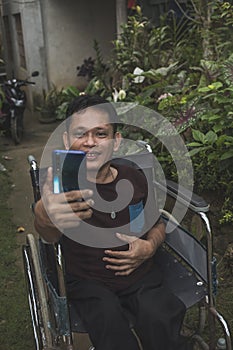 A man with a disability caused by childhood polio takes a selfie of himself with his cellphone while at his home