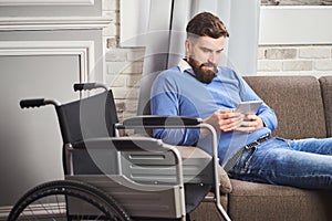 Man with disability resting on a couch and using a tablet computer