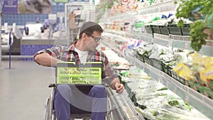 Man with a disability in a wheelchair chooses the goods in the shopping in the supermarket close up