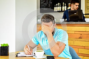 Man disappointed desperate face sit cafe with mug of coffee and notepad. Headache and stress. Deadline coming search