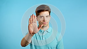 Man disapproving with NO hand sign gesture. Denying, rejecting, disagree, portrait of guy or student on blue background