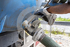 The man is disconnecting a 4 inch PVC suction hose to the flange fitting on the trucks tank.