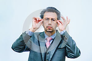 A man with disheveled hair in a business suit adjusts his glasses