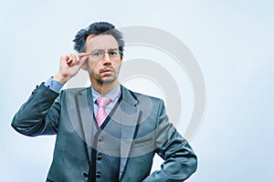 A man with disheveled hair in a business suit adjusts his glasses