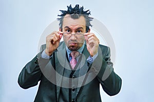 A man with disheveled hair in a business suit adjusts his glasses