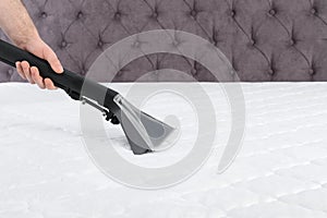 Man disinfecting mattress with vacuum cleaner, closeup.