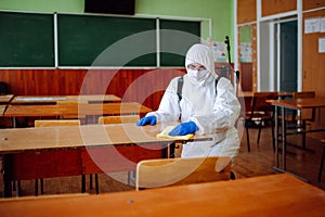 A man from disinfection group cleans up the desk at school with a yellow rag. Professional worker sterilizes the classroom to