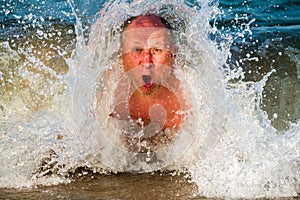 man dives in the waves with foam surprised breathes air through his mouth