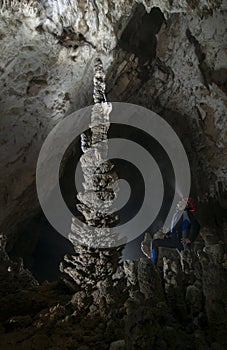 Man in diving wet suite admiring big stalagmite in