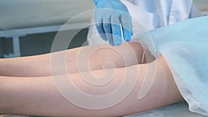 Man doctor acupuncturist in gloves inserts acupuncture needle to woman`s legs.