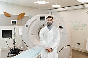 Man doctor in CT scan computed tomography room in medical clinic. Handsome bearded doctor in medical robe with computed