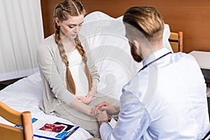 Man doctor reassuring upset pregnant woman sitting on hospital bed