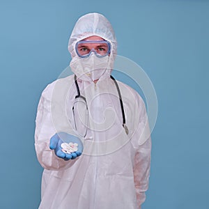Man in doctor uniform with pills in hands on blue studio background