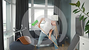 Man does the cleaning and imagines himself a rock star, plays the broom like a guitar.