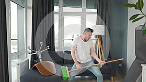 Man does the cleaning and imagines himself a rock star, plays the broom like a guitar.