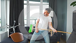 Man does the cleaning and imagines himself a rock star, plays the broom like a guitar.