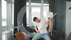 Man does the cleaning and imagines himself a rock star, plays the broom like a guitar. Slow motion
