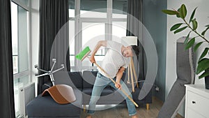 Man does the cleaning and imagines himself a rock star, plays the broom like a guitar. Slow motion