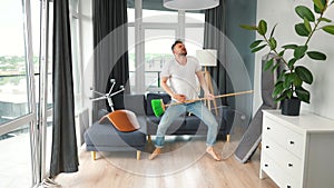 Man does the cleaning and imagines himself a rock star, plays the broom like a guitar. Slow motion