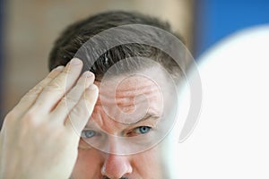 Man does gel hair styling in front of mirror.