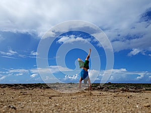 Man does Handstand on beach with clouds in the sky