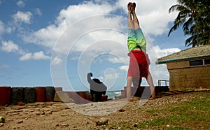 Man does Handstand at beach park next to black dog with ocean wave in the distance at Leahi Beach Park