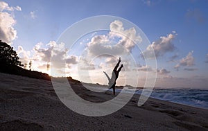Man does one hand Handstand on beach at sunset