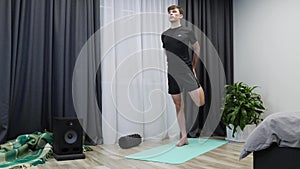 Man does stretch exercises before workout. Young athletic male doing fitness exercises on yoga mat. Boy in black sportswear stretc