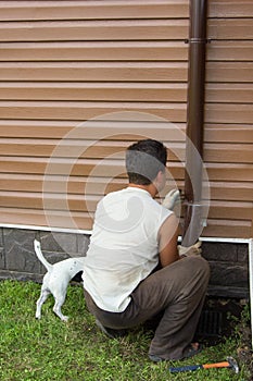 Man with a dog sets drainpipe on the wall