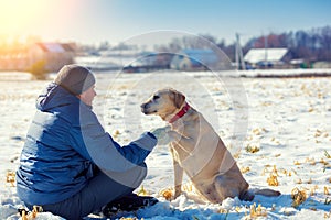 A man and the dog sit on a snowfield near the village