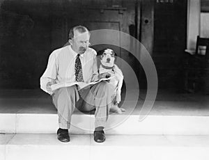 Man and dog sitting on the steps reading the newspaper