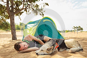 Man with Dog by tent under a tree on a sandy beach