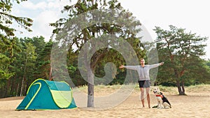 Man with Dog by tent under a tree on a sandy beach