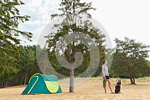 Man with Dog by tent under a tree on a sandy beach