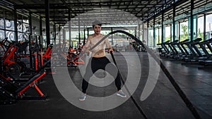 Man doing battle ropes exercise in a fitness gym. Shirtless fitness young sports man training .work out healthy. exhausted, tired