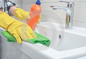 Man doing chores cleaning bathroom at home. Cropped view of woman in rubber gloves wet rag near detergent on sink in bathroom.