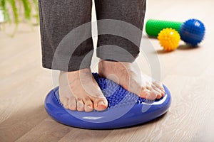 Man doing flatfoot correction gymnastic exercise balancing on massage cushion at home