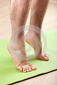 Man doing flatfoot correction gymnastic exercise standing on toes at home