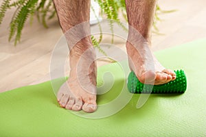 Man doing flatfoot correction gymnastic exercise using massage roller at home