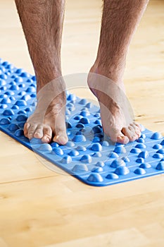 Man doing flatfoot correction gymnastic exercise walking on massage mat at home