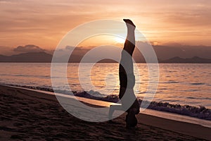 Man is doing his morning exercises on the beach during orange sunrise by the sea