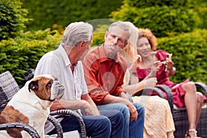 Man Doing Impression Of Pet Bulldog Sitting Outdoors With Friends At Home